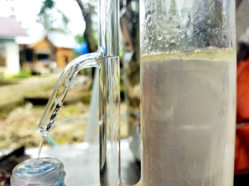 Close-up of a glass distillation setup with clear condensate dripping into a collection container.