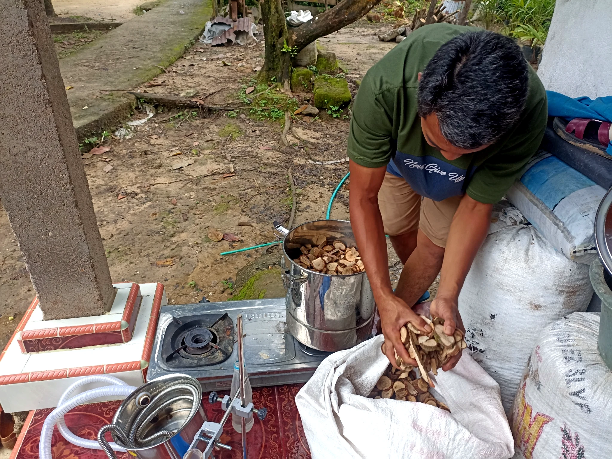 Seorang peserta memasukkan potongan bahan tumbuhan ke dalam tabung penyulingan logam di luar ruangan.