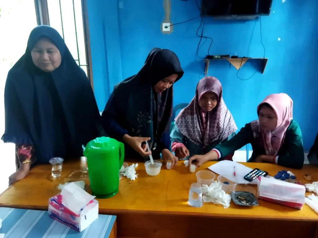 Four women working with small containers, measuring cups and training materials at a table.
