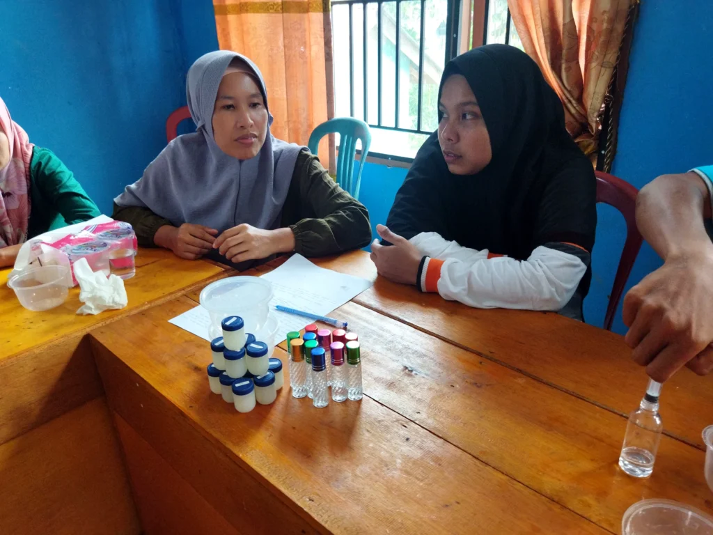 Community members seated together while examining plant material samples during an essential-oil discussion in Lubuk Bigau.