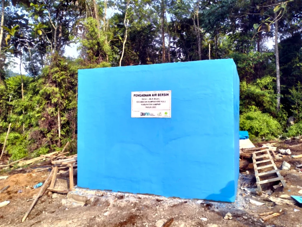 Blue water storage tank with a project sign in a forested area.