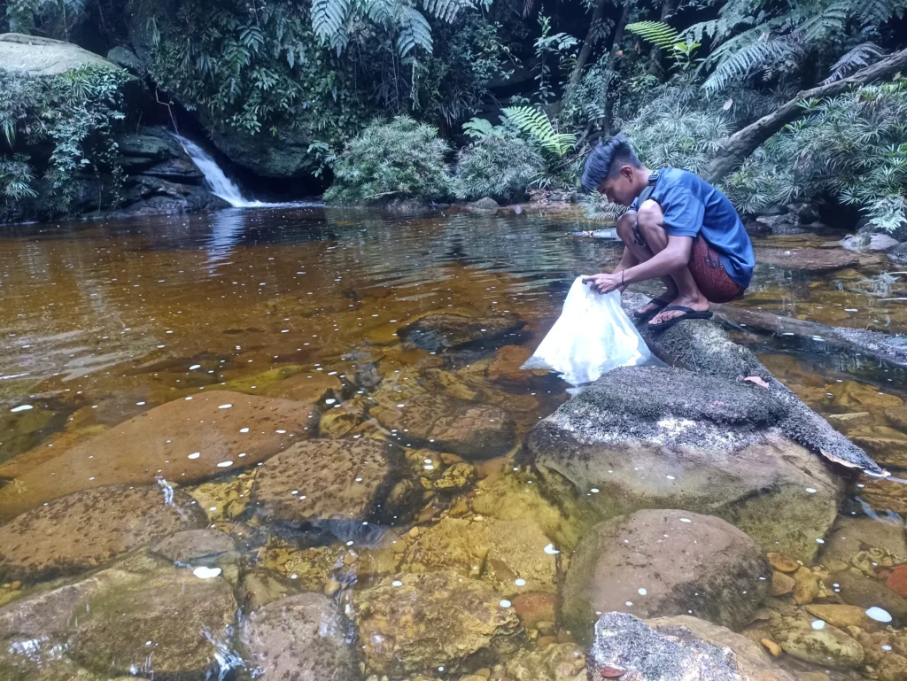 People standing beside a forest river pool during a juvenile fish release in Lubuk Bigau.