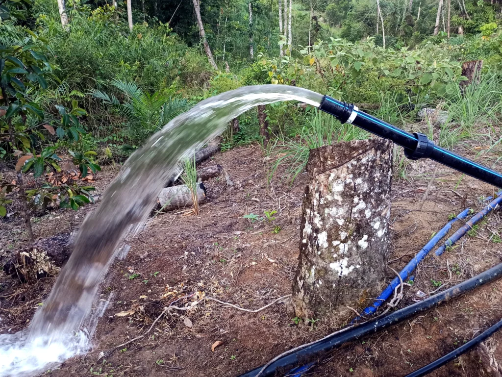 A strong stream of water flowing from the end of a black pipe.