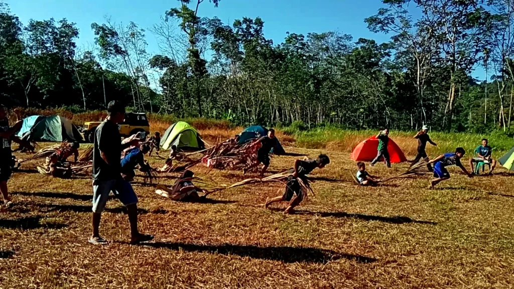 People taking part in a traditional outdoor game beside tents at a campsite.