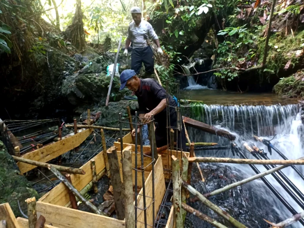 Several workers constructing a timber-and-steel structure within a small forest stream.