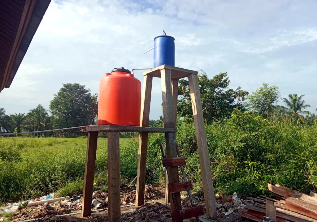 Orange and blue water tanks mounted on two elevated support towers in the school grounds.