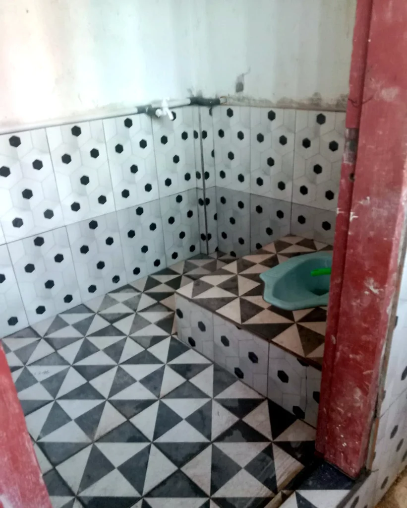 A tiled toilet room with a squat toilet and water pipes along the wall.