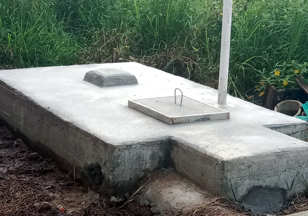 A low concrete sanitation structure with two inspection covers in a grassy area.