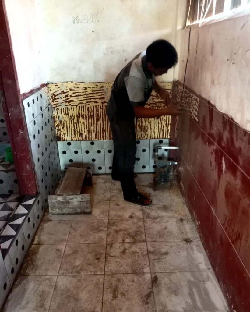 A worker installing wall tiles inside a toilet room.