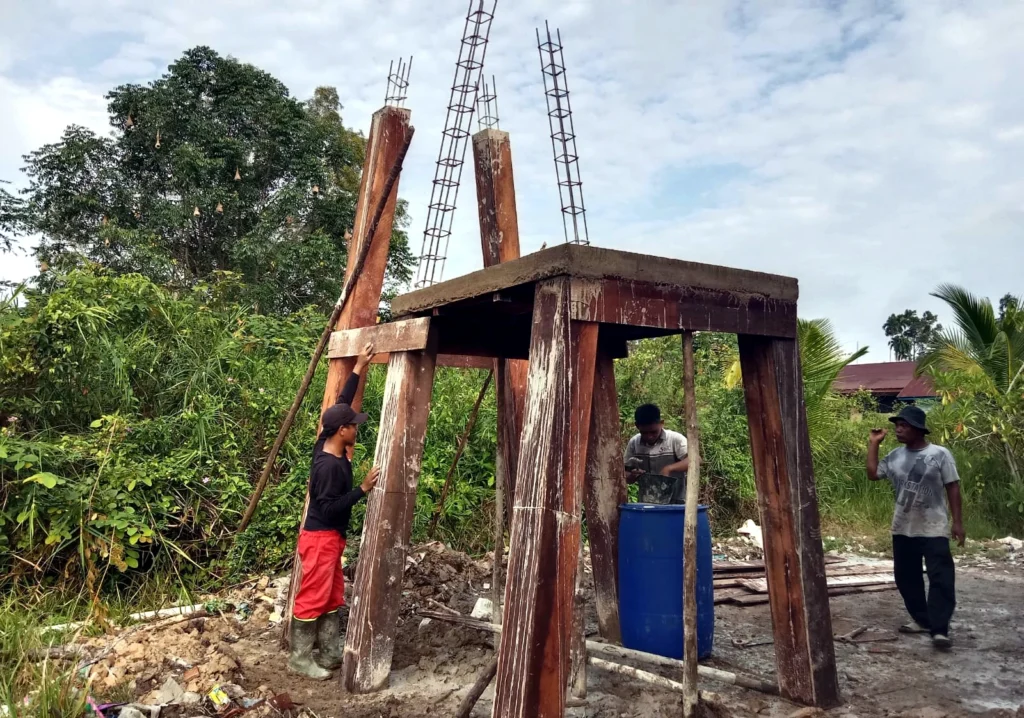 Three workers beside a concrete structure with timber formwork for an elevated water tank.